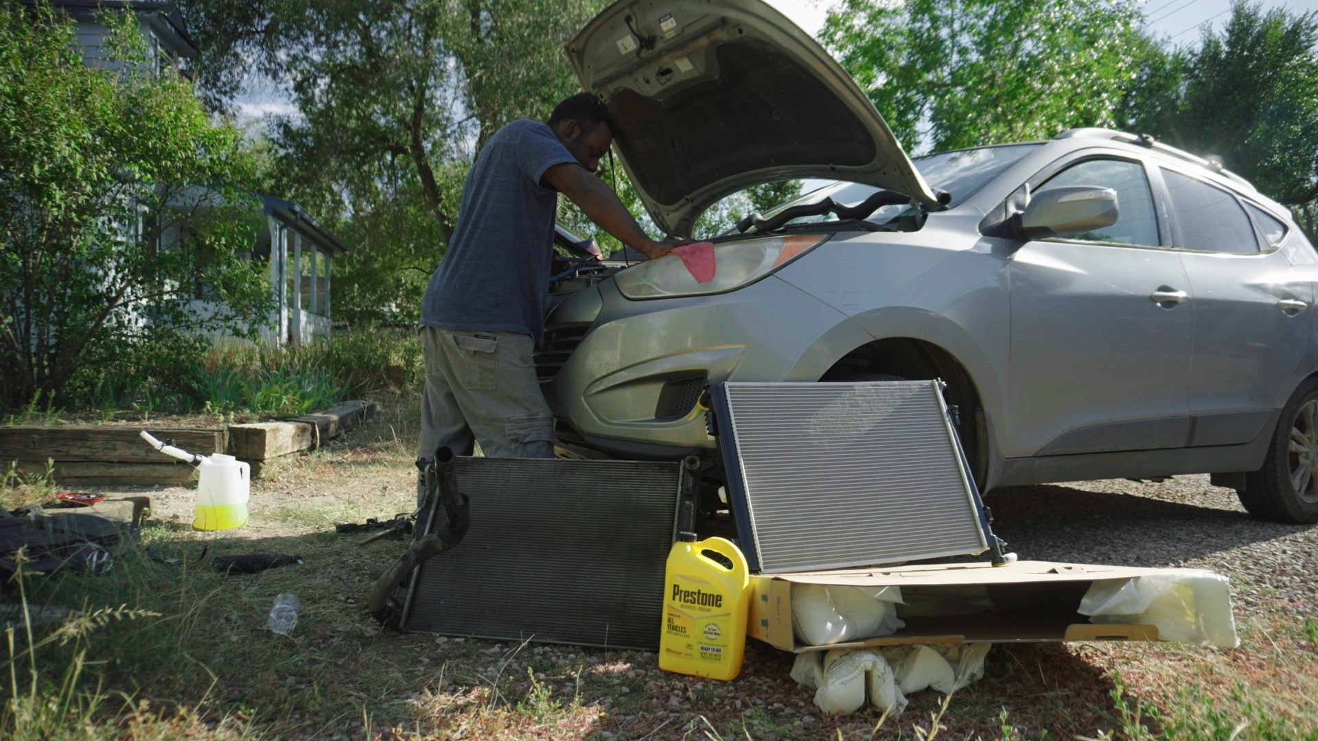 Mobile mechanic working under an open hood with replacement cooling components in the foreground